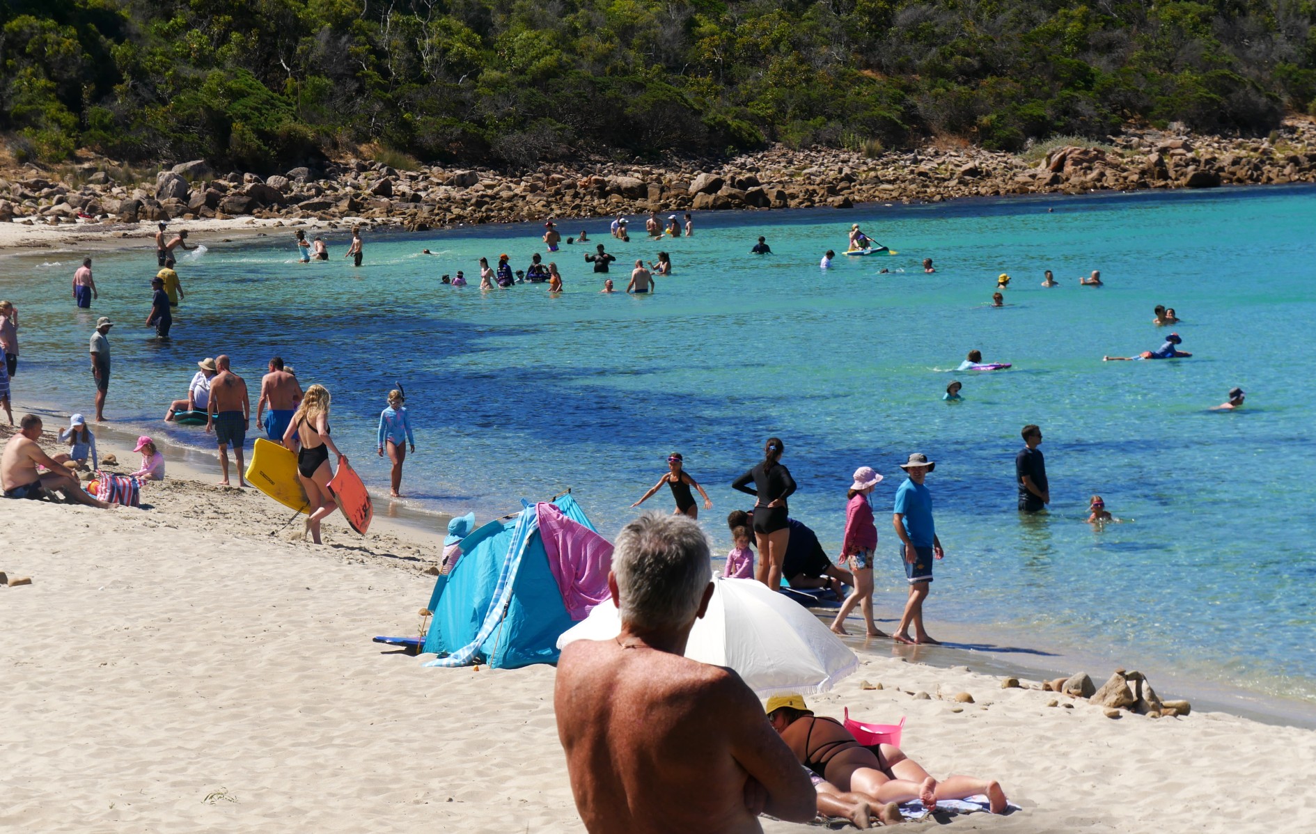 Pessoas nadando, deitadas na praia e curtindo a praia.
