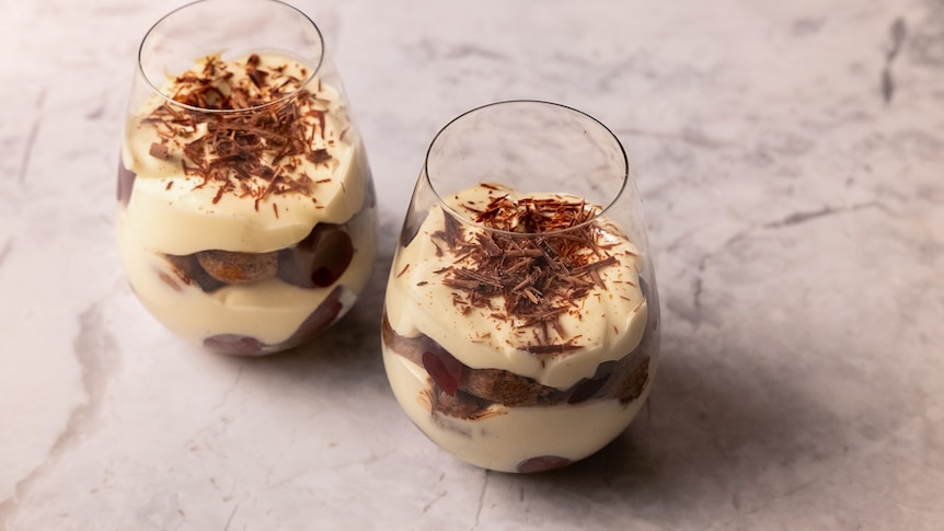 Two glasses contain layers of cream, topped with grated chocolate.
