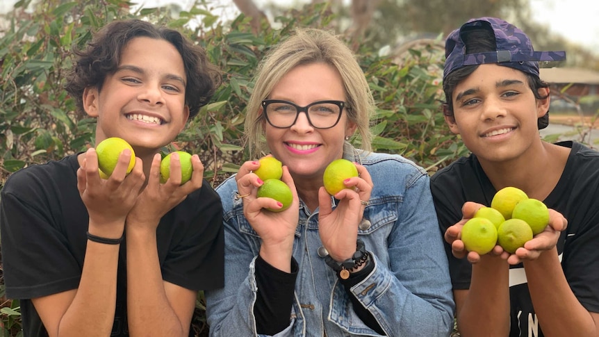 Three people including two young indigenous boys and a woman holding limes and smiling