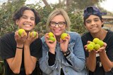 Three people including two young indigenous boys and a woman holding limes and smiling