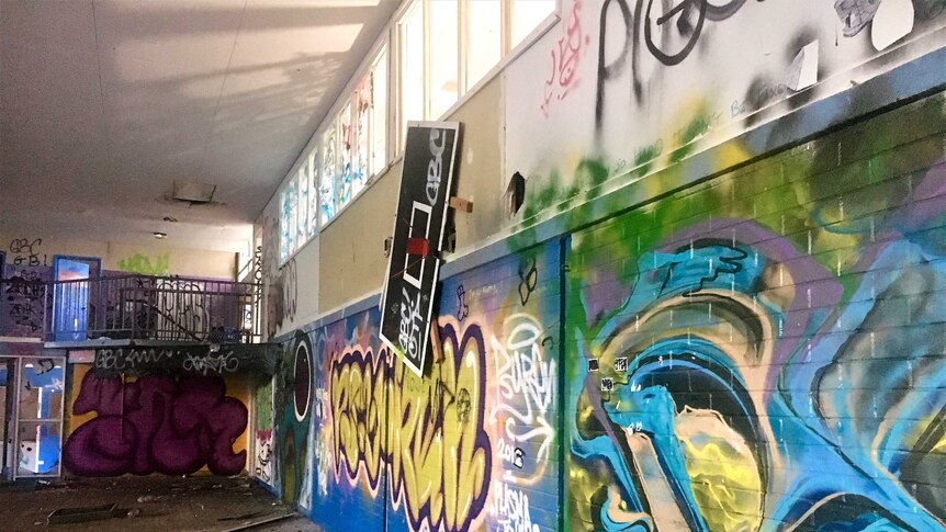 A vandalised room with graffiti covering walls, glass on floor and damaged basketball hoop.