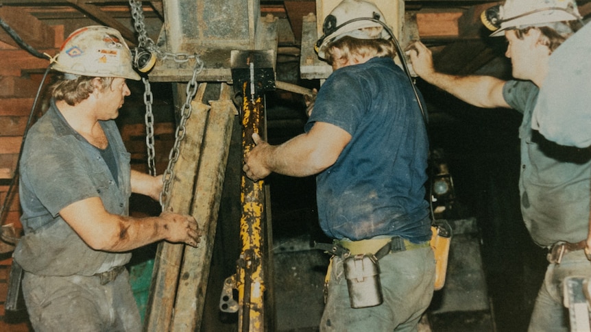 Three men look down a shaft.