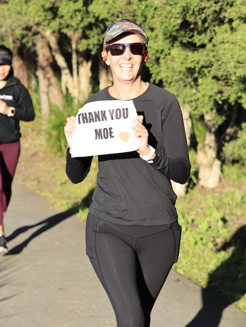 A woman holds up a sign that says "THANK YOU MOE" as she runs past