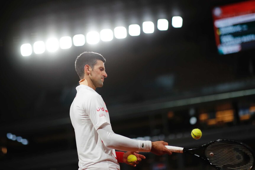 The bright lights shine on Novak Djokovic as he knocks a ball to himself with his racquet