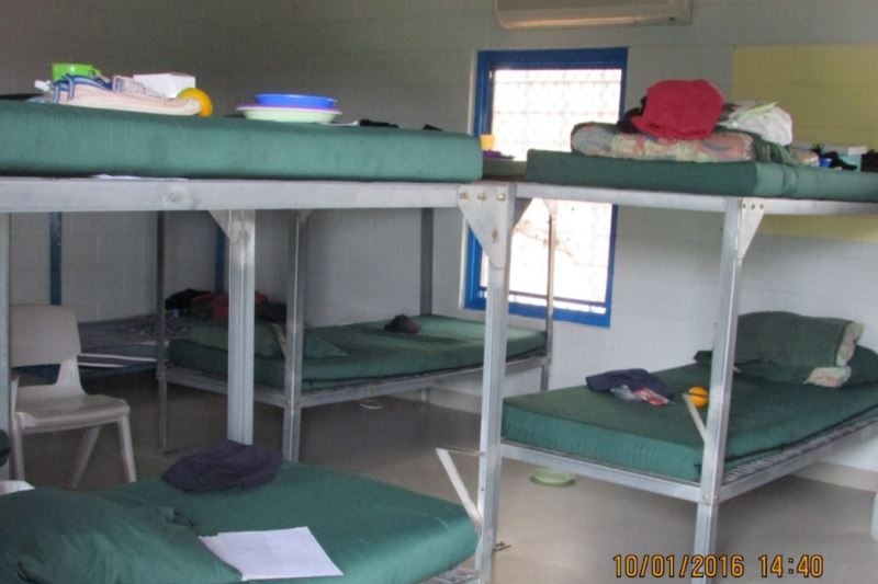 Steel bunkbeds with green mattresses in a grey prison room.