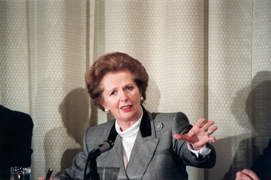 A 1980s photo of a middle-aged woman sitting in front of a microphone and gesturing