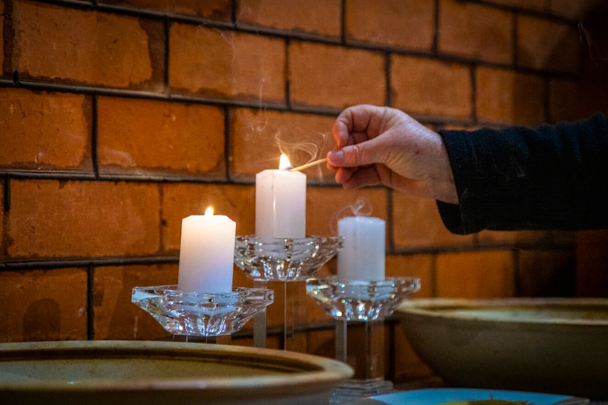 A hand lights candles against a brick church interior wall.
