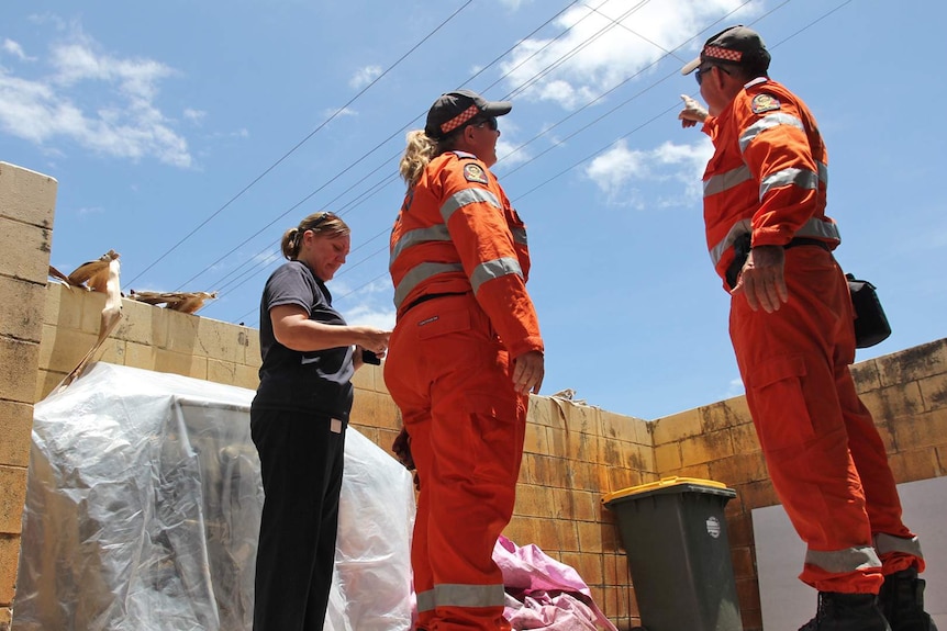 SES staff point at powerlines in a suburban yard. The yard also has a barbecue, wheelie bin and building materials.