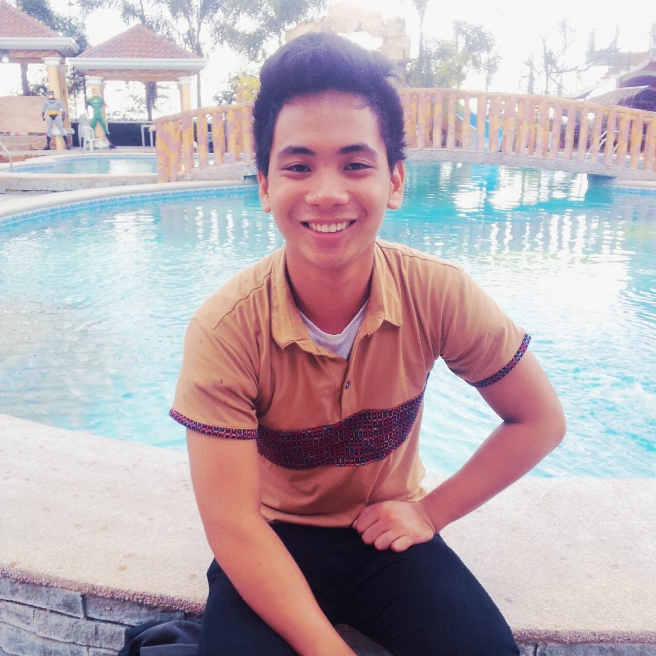 Un joven se sienta al borde de una piscina y sonríe.