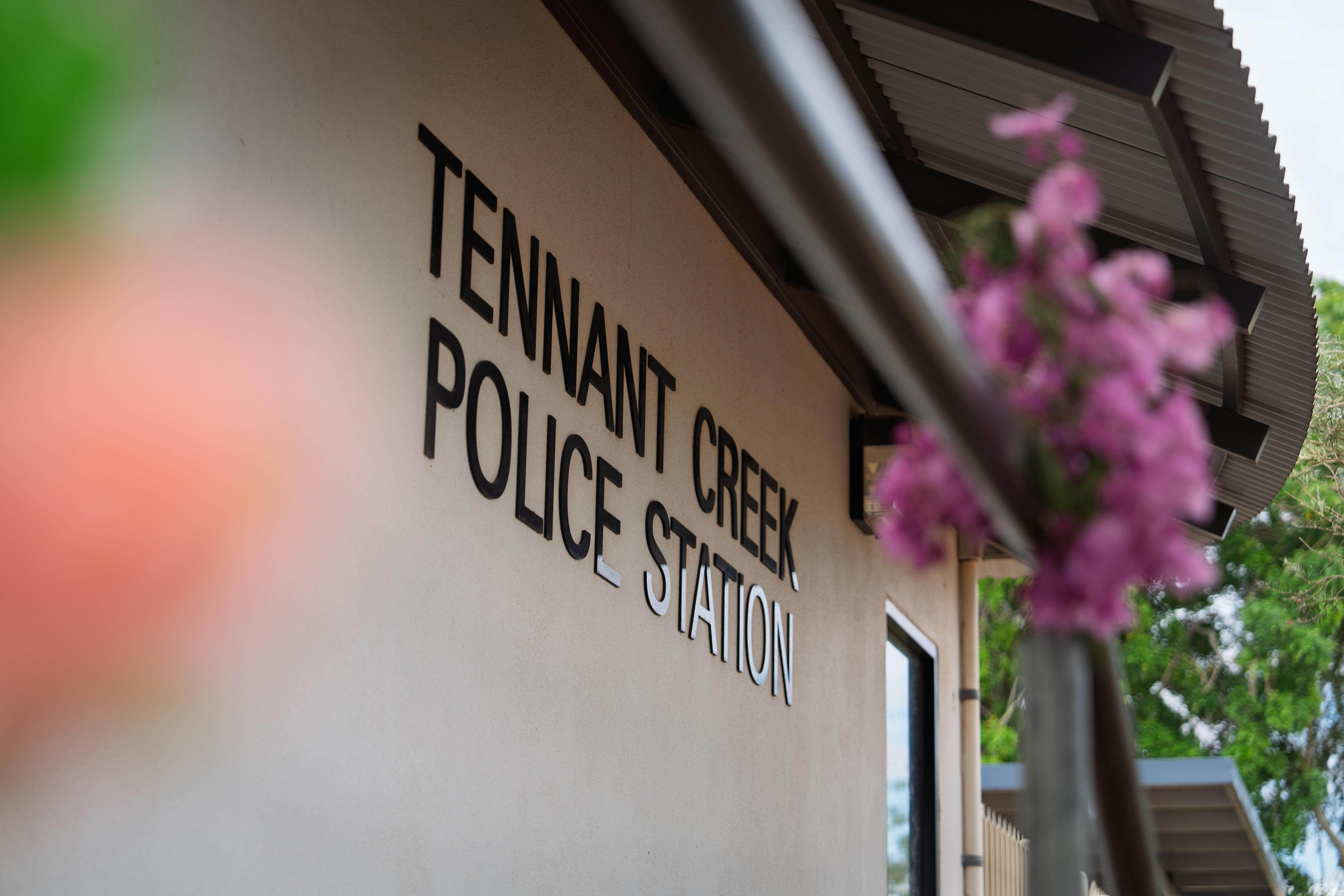 Placa da Delegacia de Polícia de Tennant Creek com homenagem a flores na grade em primeiro plano 