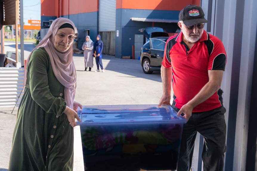 Two people lift a big plastic box together