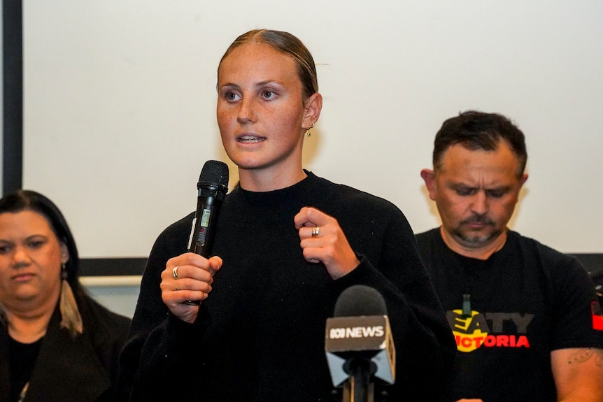 Zali Mifsud appears determined as she speaks into a microphone at a community event.