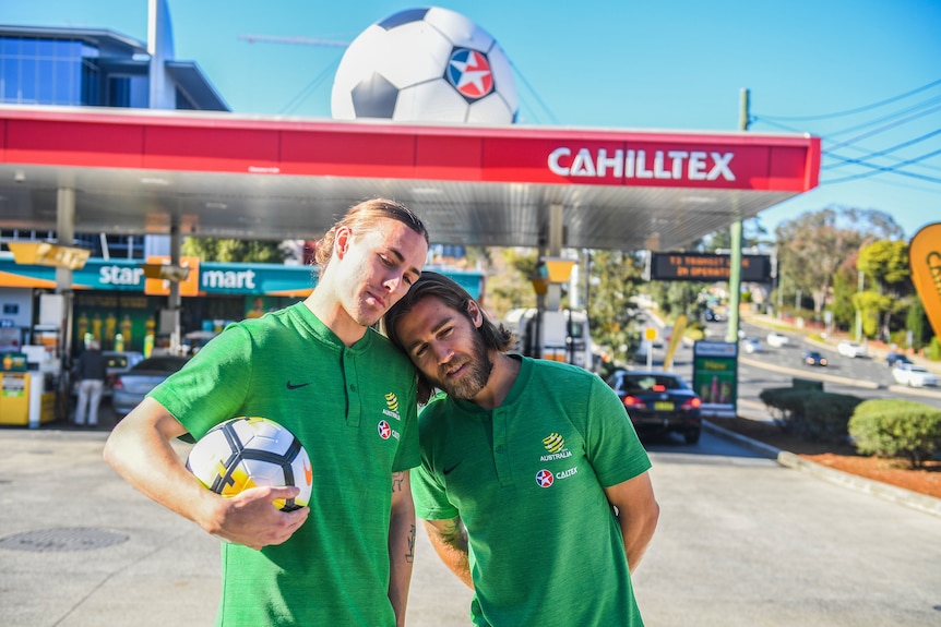 Jackson Irvine and Josh Brillante pose in front of Cahilltex sign