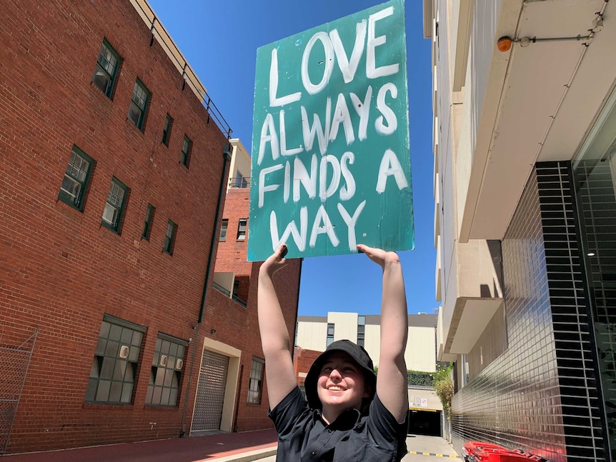 A refugee holds up a sign that says love always finds a way.