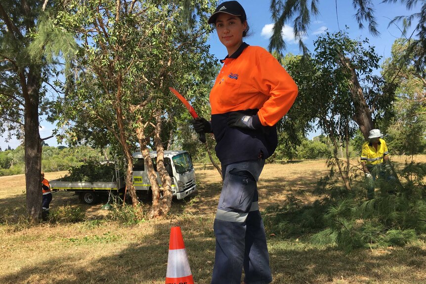 A woman wearing orange hi-vis clothing stands in a garden.