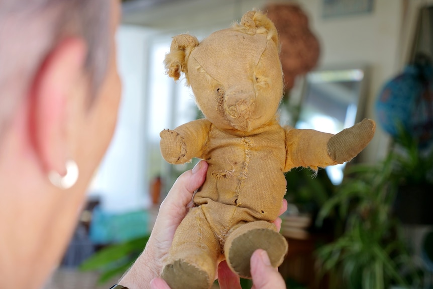 Woman holding teddy up, seeing all teddy's worn parts
