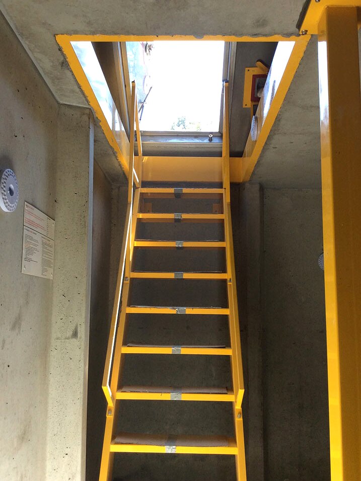 A yellow staircase leads out of a concrete room into open air