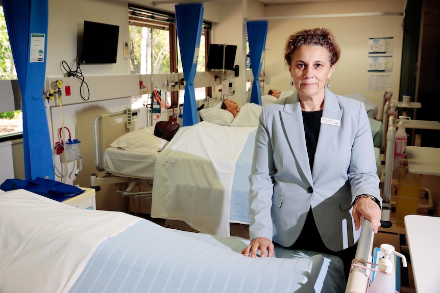 Woman stands next to bed with dummy in it in a university nursing practice lab