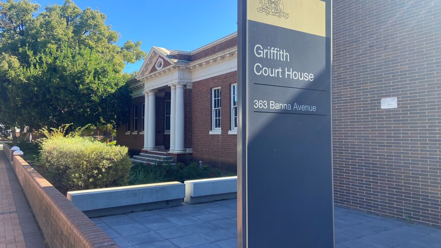 A sign that reads "Griffith Court House" out the front of a Federation-style brick building with columns at the entrance.