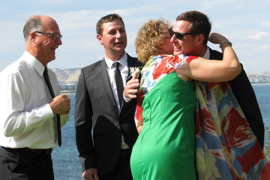 Three men in formal suits as a woman in a dress hugs one of the men