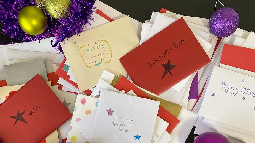 A photograph shows piles of colourful envelopes and Christmas decorations laid out on a table.