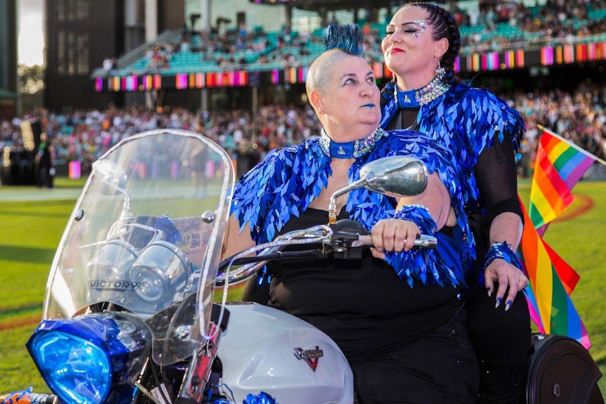 Two women wearing blue tassels on a motorcycle