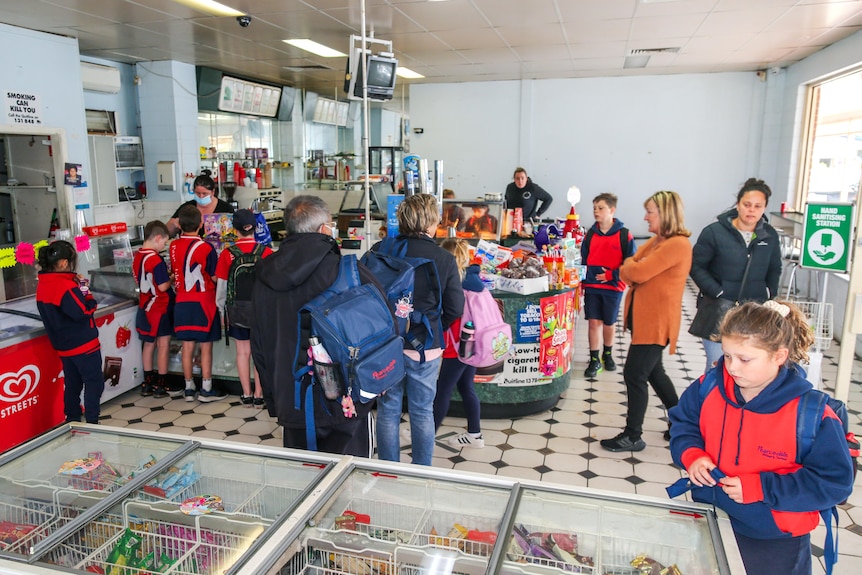Customers crowd a counter at a milkbar. A child in the foreground