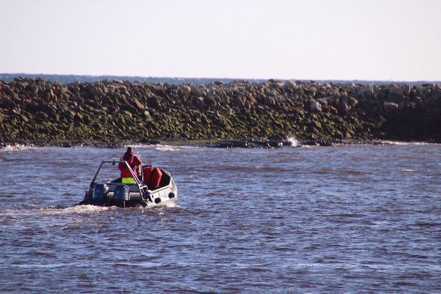 A person wearing high visibility clothing drives a small inflatable boat.