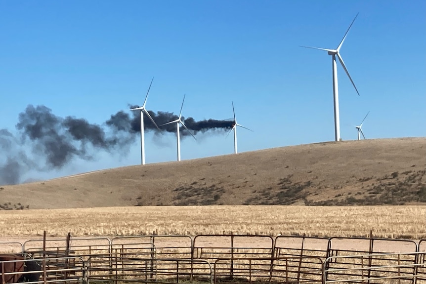 A series of wind turbines among farmland with black smoke coming from one of them