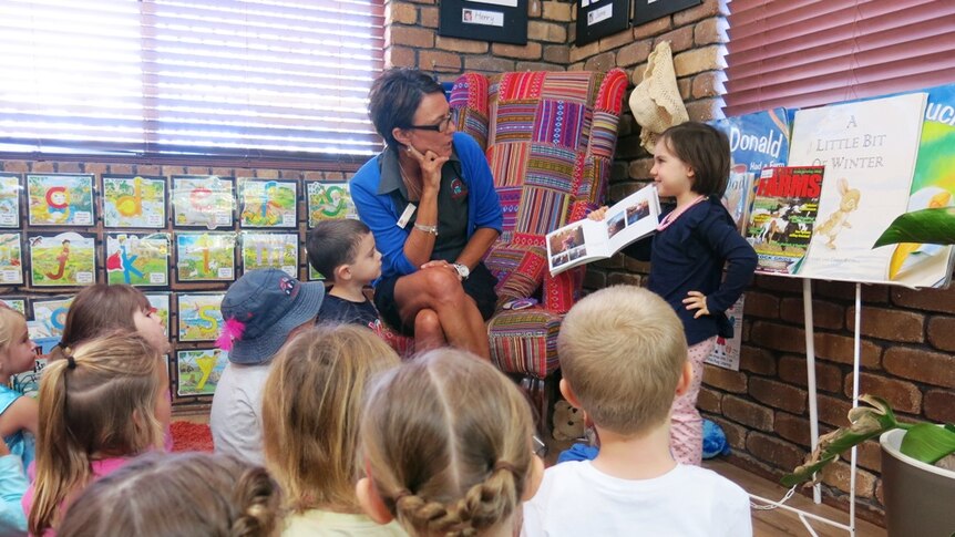 Jasmine Smith standing in front of her kindy class reading a book to them.