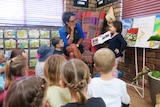 Jasmine Smith standing in front of her kindy class reading a book to them.