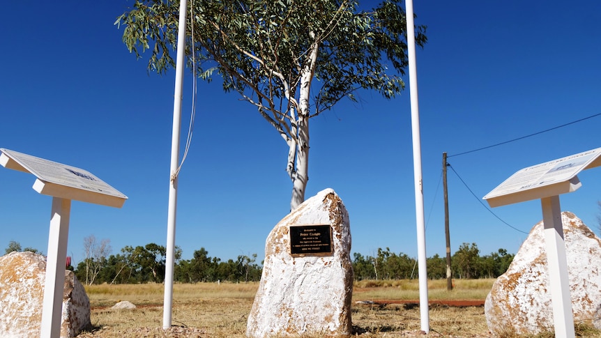 A war memorial in the form of a white stone with plaque underneath a gum tree