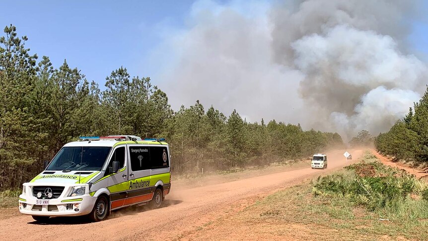 A procession of ambulances heading from Pechey bushfire with a smoke cloud behind them.