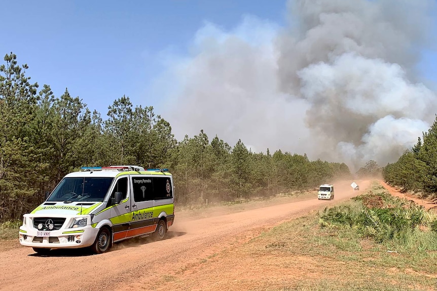 A procession of ambulances heading from Pechey bushfire with a smoke cloud behind them.