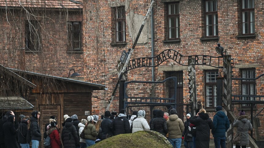 Small crowd wearing jackets in front of 'Arbeit Macht Frei' sign at the main entrance gate of Auschwitz