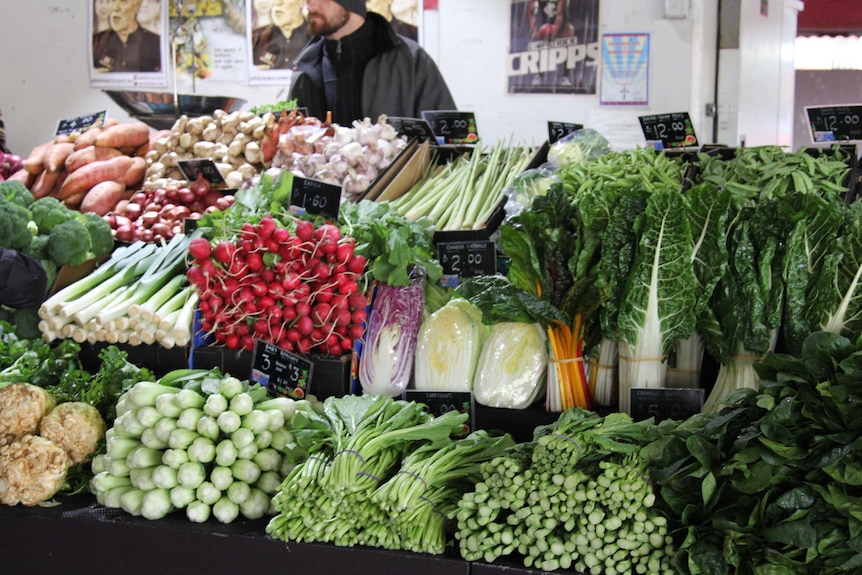 A man stands behind a stall of fruit and vegetables.