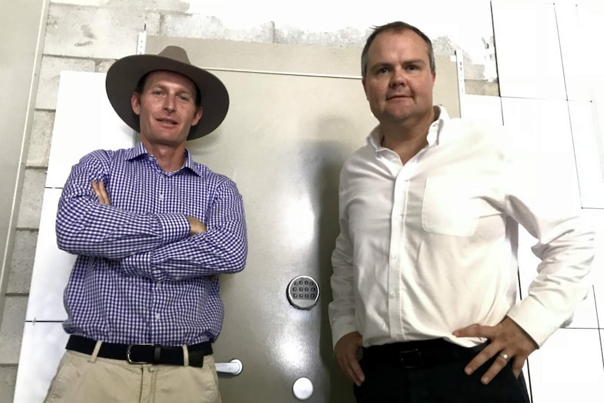 The two men look down at the camera with the steel vault door behind them.