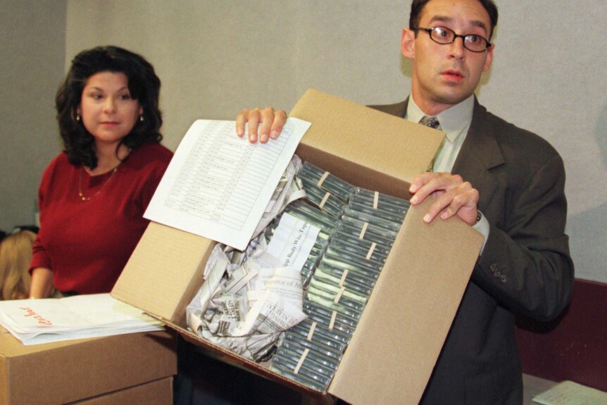 A man holds up a box full of casette tapes.