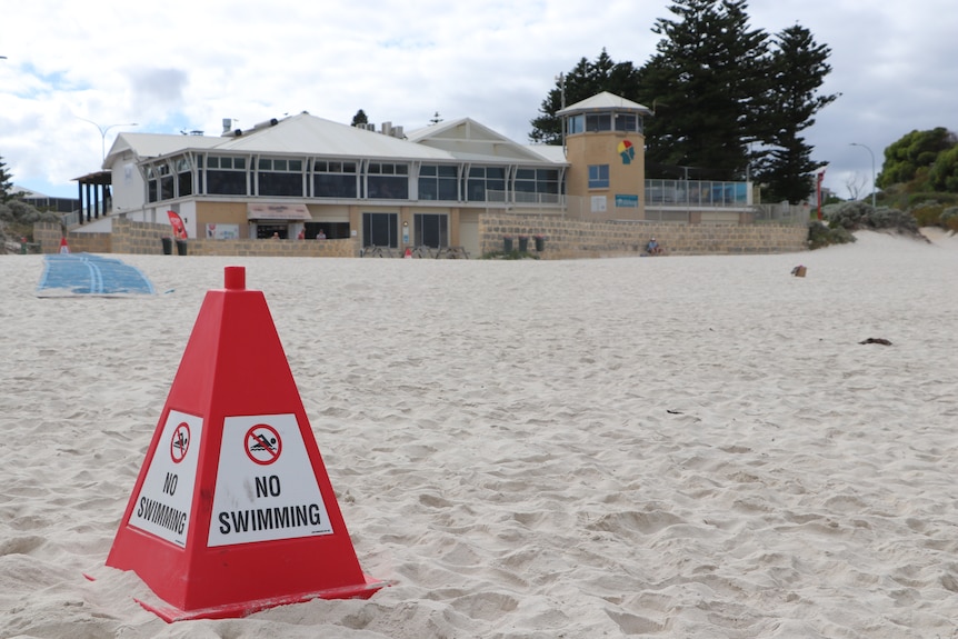 A ;no swimming' sign at a beach, with a surf club in the background