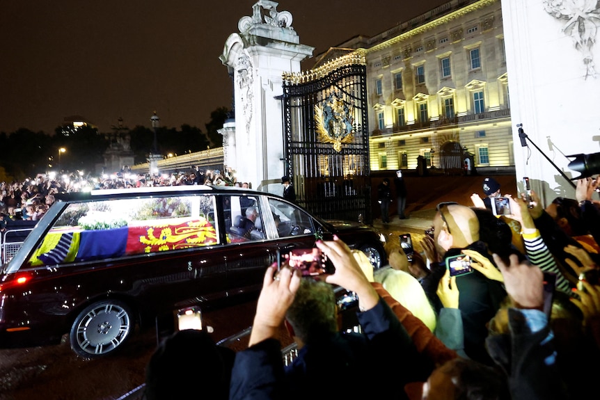 Crowds take photoraphs as Queen Elizabeth's coffin is driven ina hearse through the gates of Buckingham Palace. 