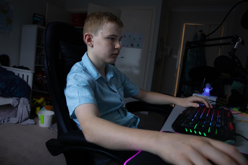 A teenage boy in a blue polo shirt sits in front of a keyboard which has light-up keys 