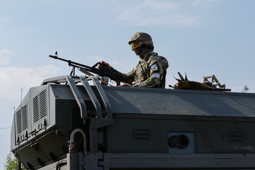 Man with gun stands on war tank 