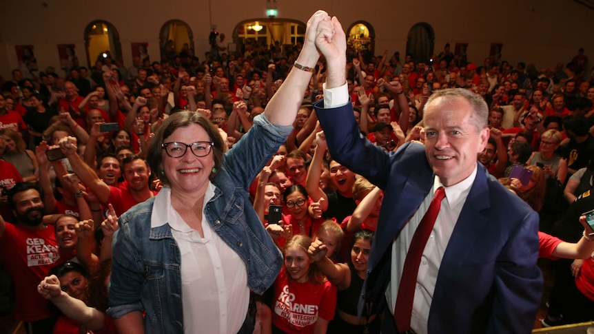 Bill Shorten and Ged Kearney join hands with a crowd of supporters behind them.