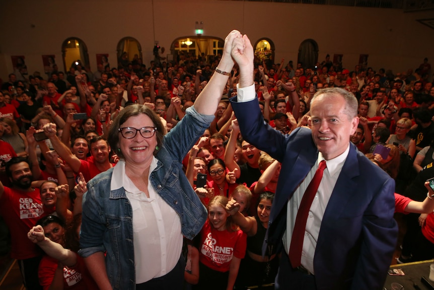 Bill Shorten and Ged Kearney join hands with a crowd of supporters behind them.
