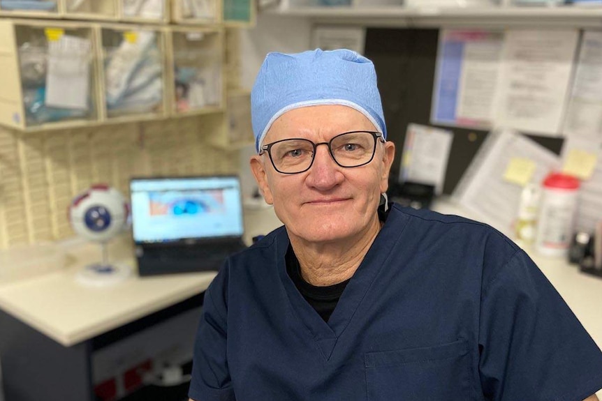 Dr Bill Glasson sits in an office dressed in surgical clothing.