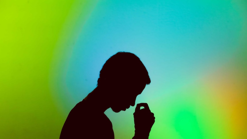 Silhouette of young man holding his head, in front of bright green / blue background
