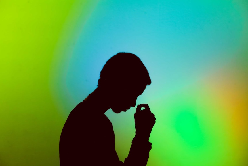 Silhouette of young man holding his head, in front of bright green / blue background