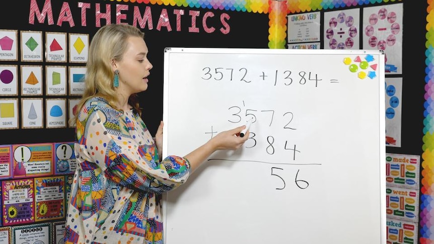 Female teacher in classroom points to equation on whiteboard