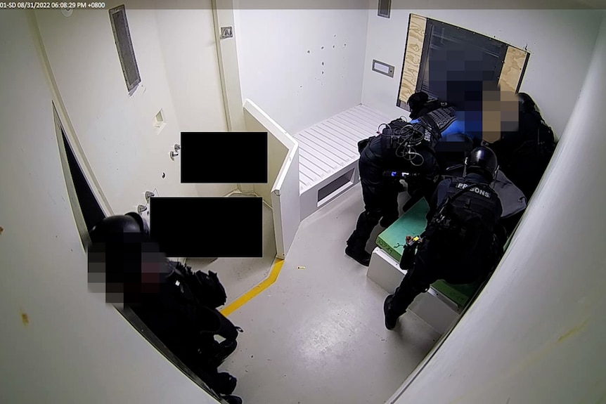 A group of unidentifiable guards on top of a detainee who cannot be seen.