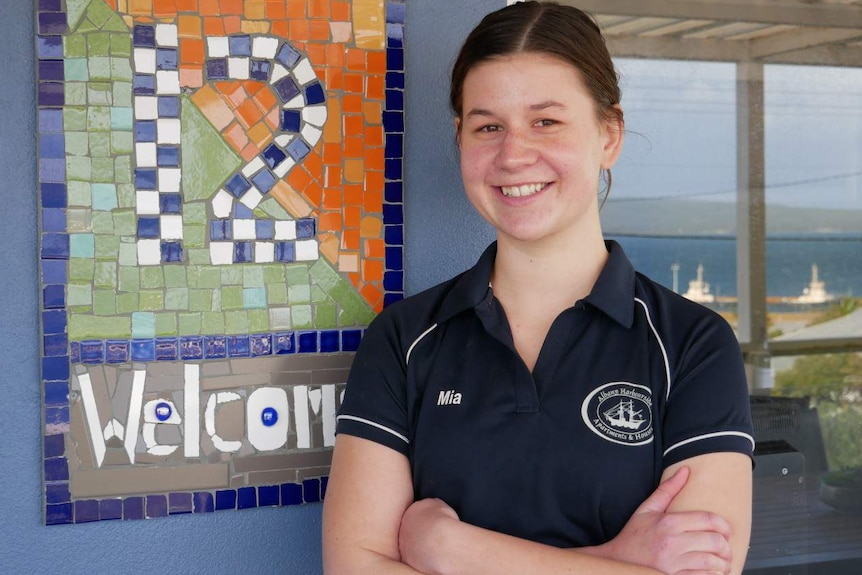A mid-shot of a young woman wearing a blue polo shirt posing for a photo smiling in front of a tiled wall motif.